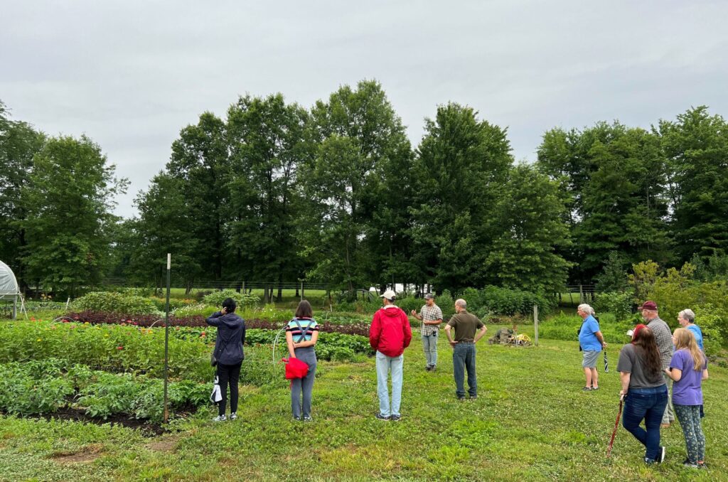 adult visitors standing outside near garden, talking to farmer