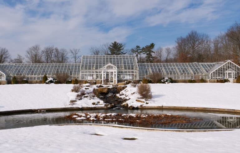 Snow-covered large Greenhouse with pond in front.