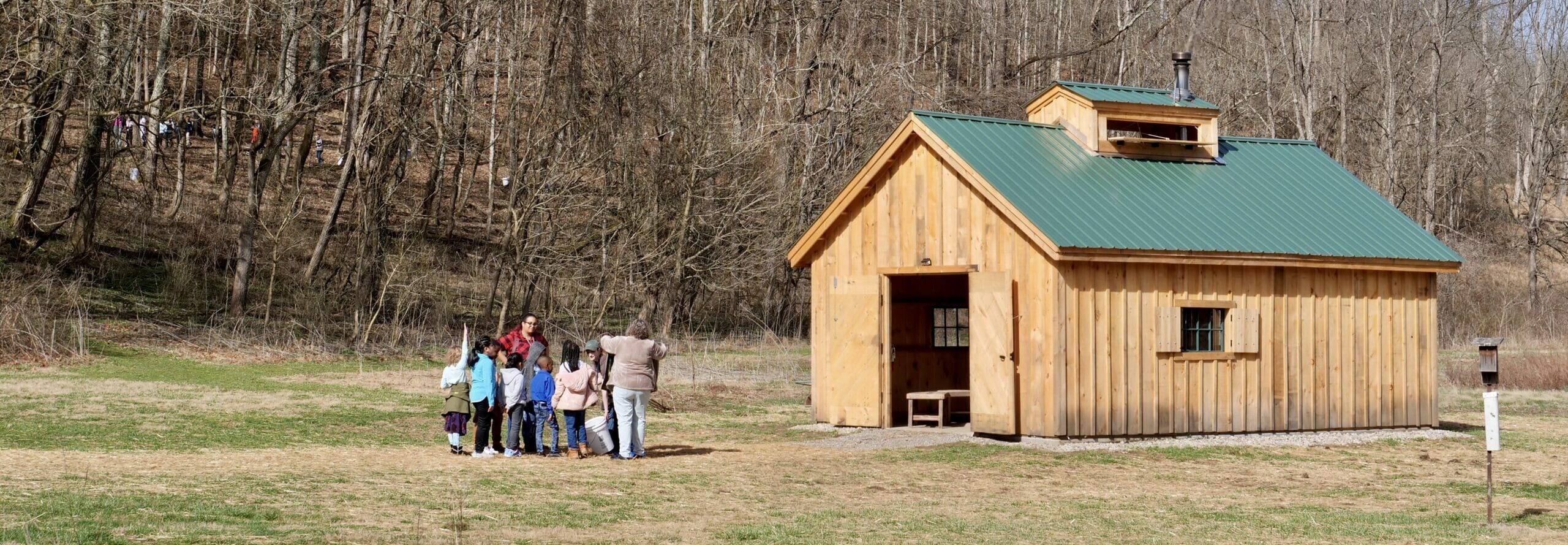 A group of children gathering outside a wooden maple sugar shake